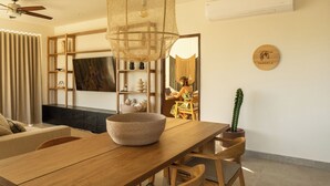 Un salon moderne avec une table à manger en bois, un grand luminaire en fibres tressées et un cactus.