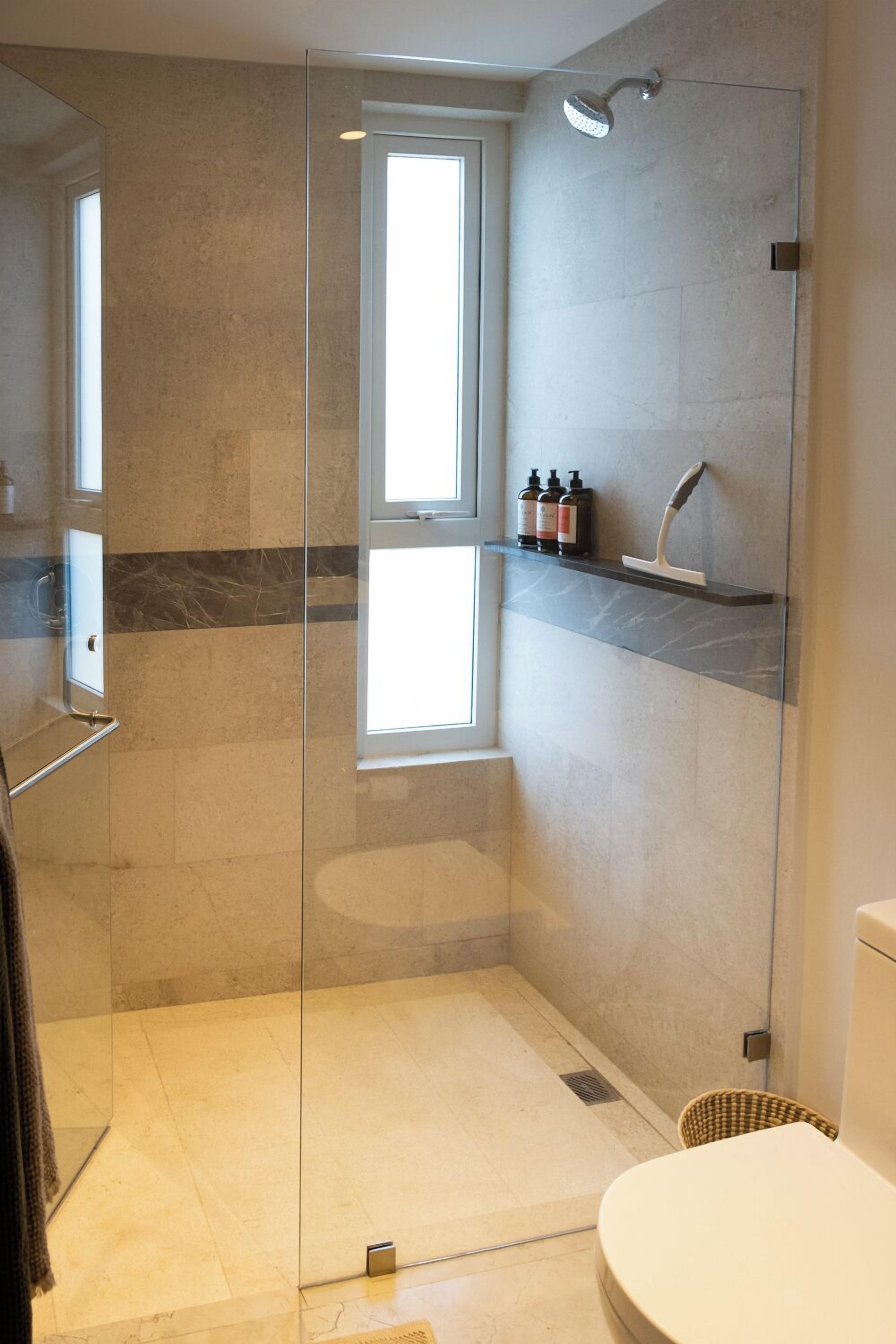 Un baño moderno con ducha de vidrio, inodoro y un ventanal pequeño.