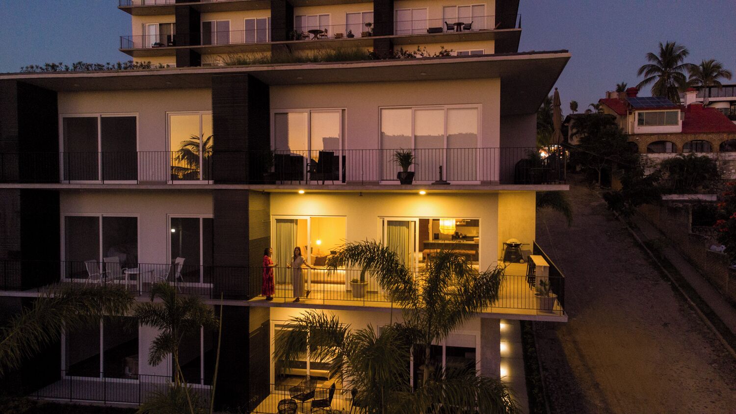Un immeuble résidentiel à plusieurs étages, doté de balcons, de grandes fenêtres et d’espaces extérieurs aménagés pour s’asseoir.