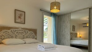 Ein ordentlich bezogenes Bett mit weißer Decke und Kissen, ein dekorativer Kopfteil, eine hängende Leuchte und ein gerahmtes Bild an der Wand.
