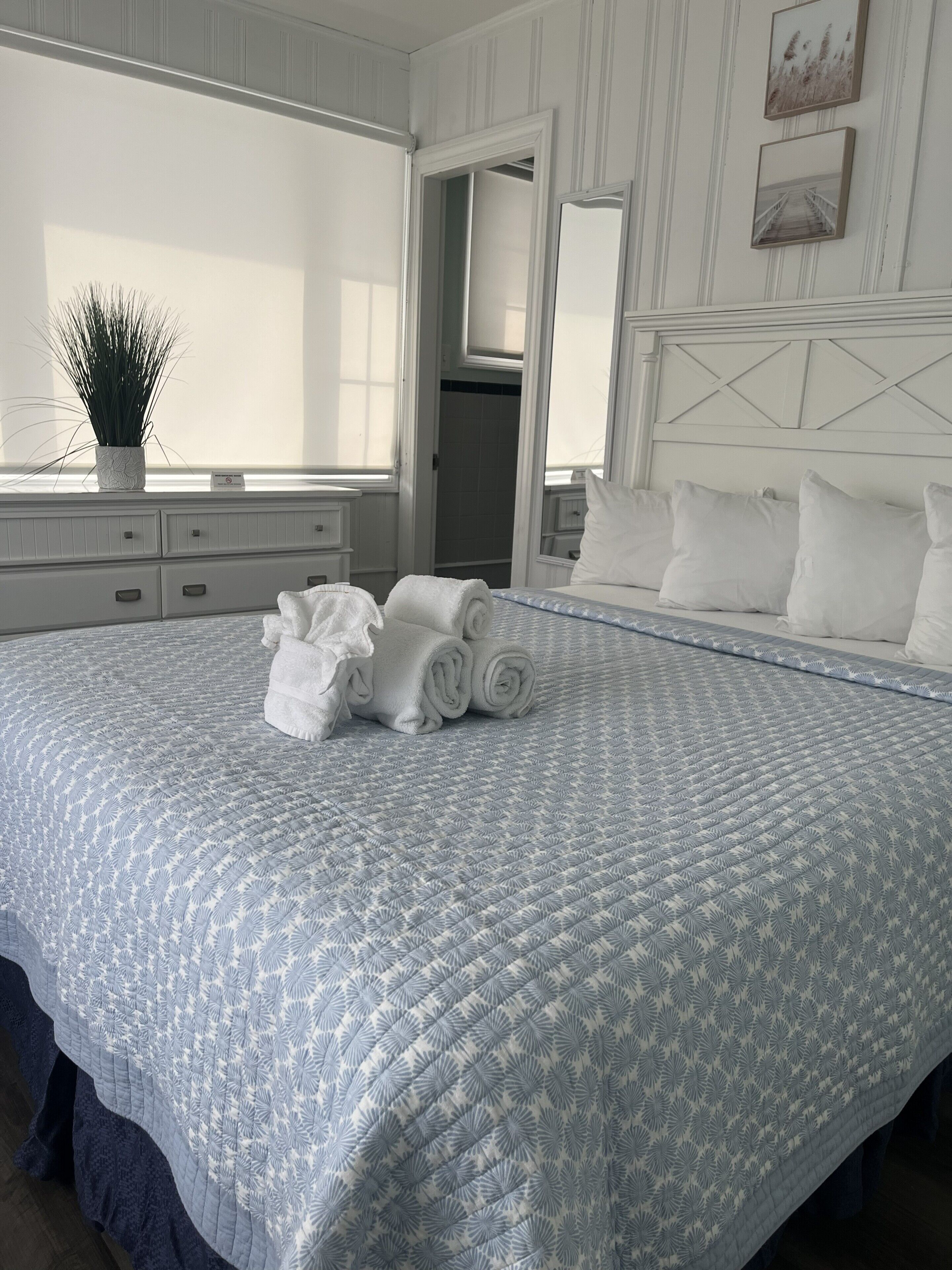 A neatly made bed with rolled towels, a potted plant, and a large window in a hotel room.