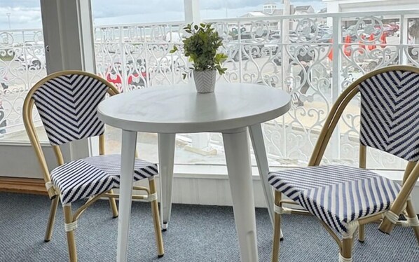 A round white table with two striped chairs, a potted plant, and a balcony with ornate white railings. - Harris Sea Ranch Beach Hotel (Hampton)