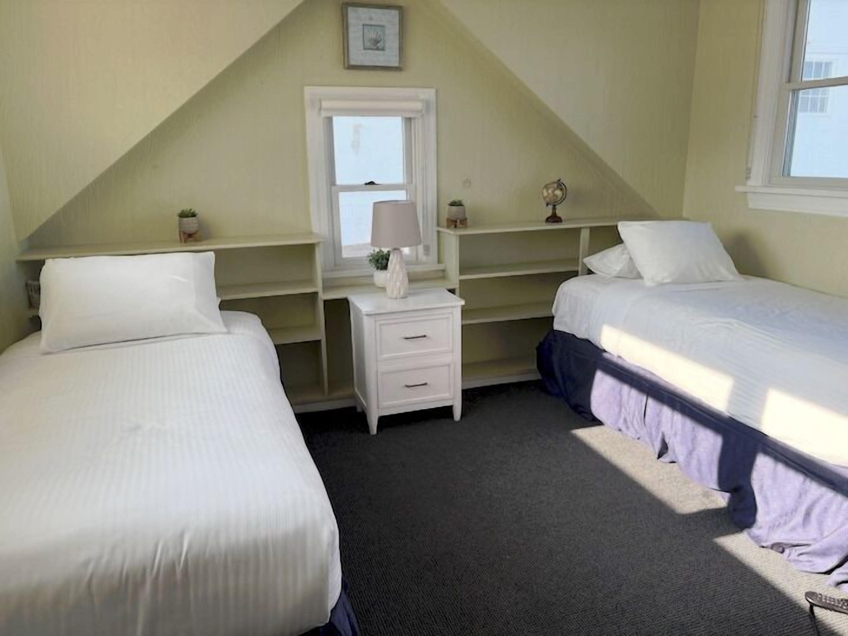 Ein Schlafzimmer mit zwei Betten, einem Schreibtisch mit Lampe und einem Fenster.