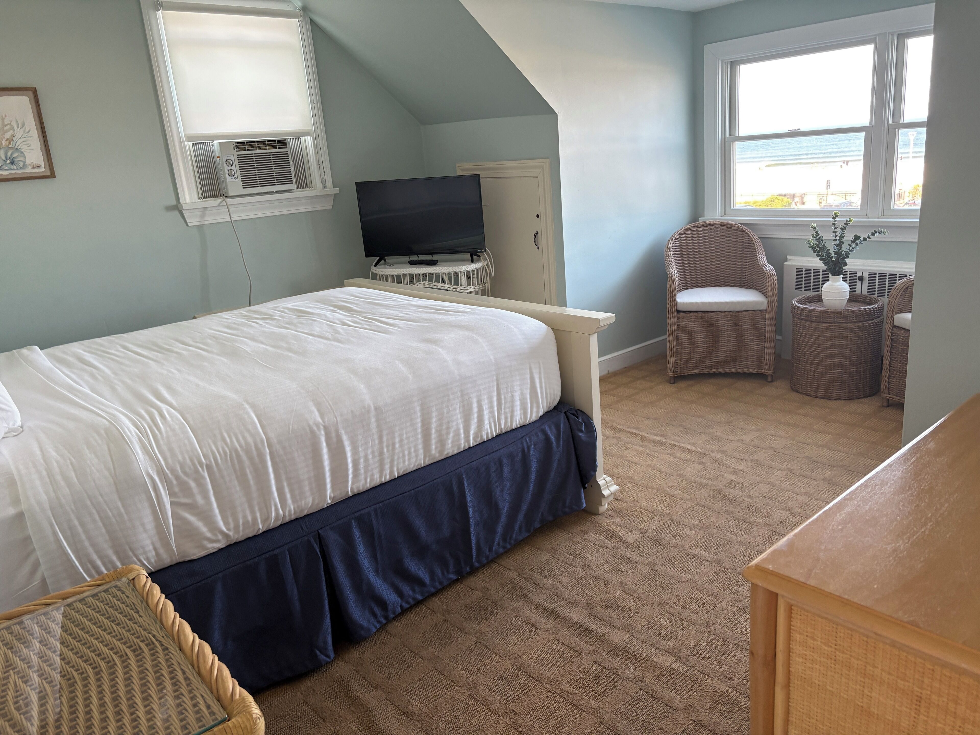 Ein Schlafzimmer mit Bett, Fernseher, Korbsesseln und Meerblick durch das Fenster.
