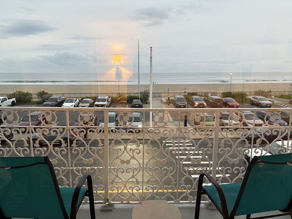 A balcony with ornate metal railings, overlooking a parking area and beach.