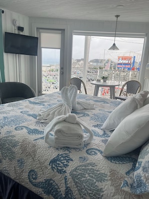 A hotel room with a bed, a chair, a table, and a view of the beach bar. - Harris Sea Ranch Beach Hotel (Hampton)