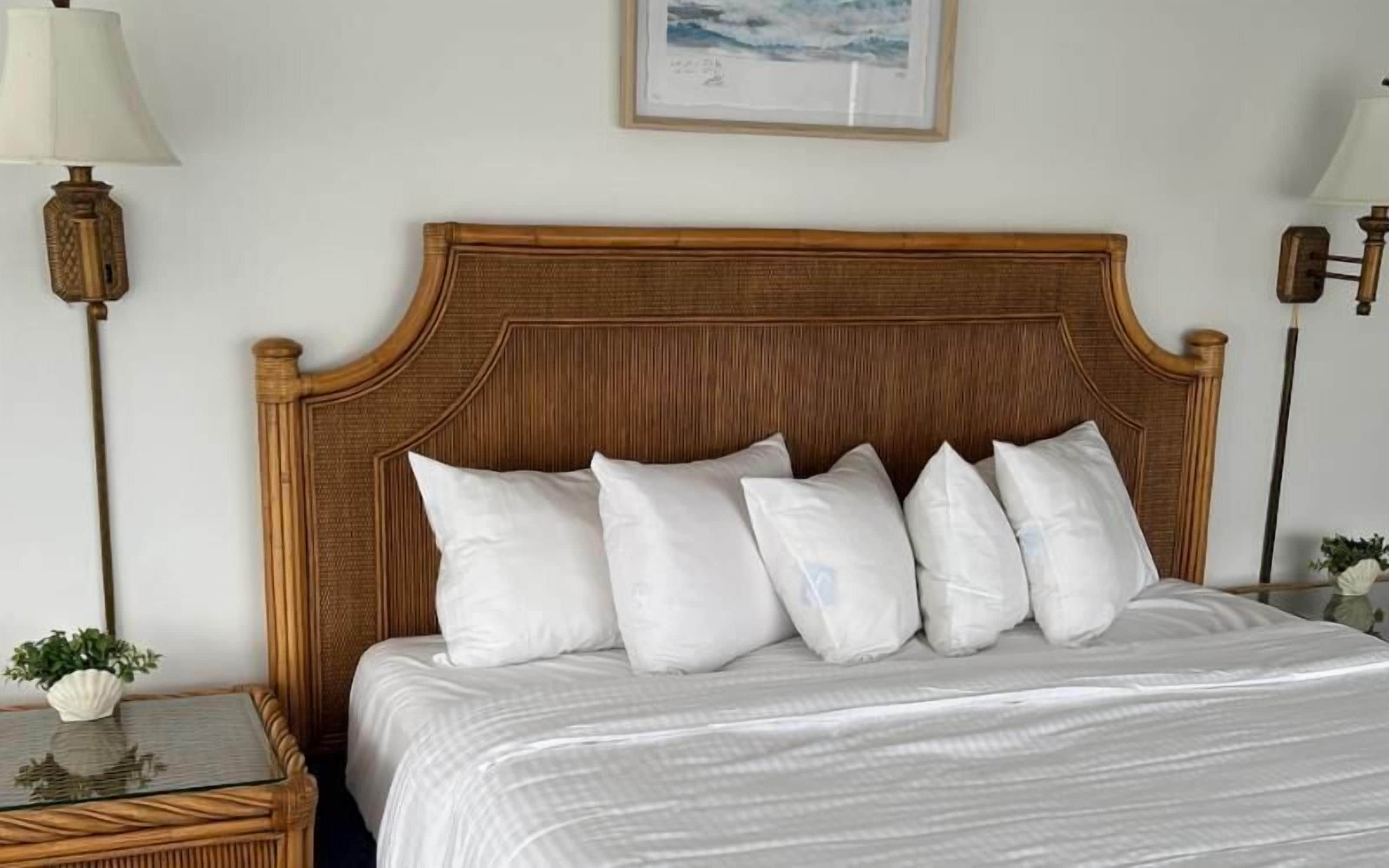 A neatly made bed with a wooden headboard, white pillows, and a glass table with a plant beside it.