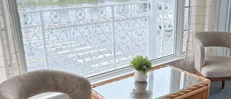 A room with a glass-top table, two armchairs, and a view of a balcony with a railing.