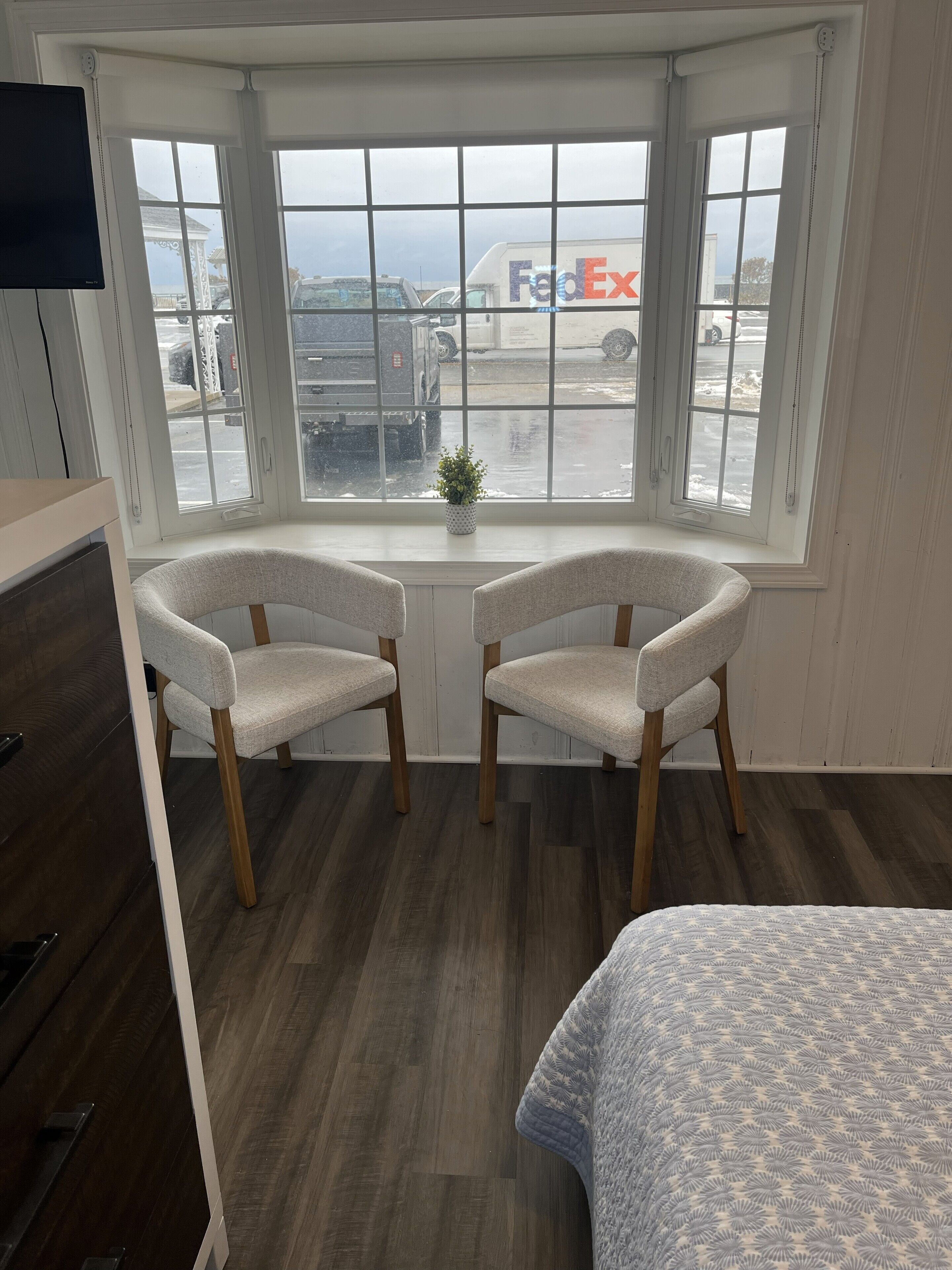 Een kamer met erker, twee gestoffeerde fauteuils, een tafeltje, een bed en een televisie.