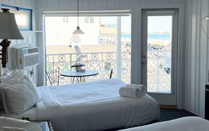 A hotel room with a bed, a table with chairs, a balcony with a railing, and a view of the beach. - Harris Sea Ranch Beach Hotel (Hampton)
