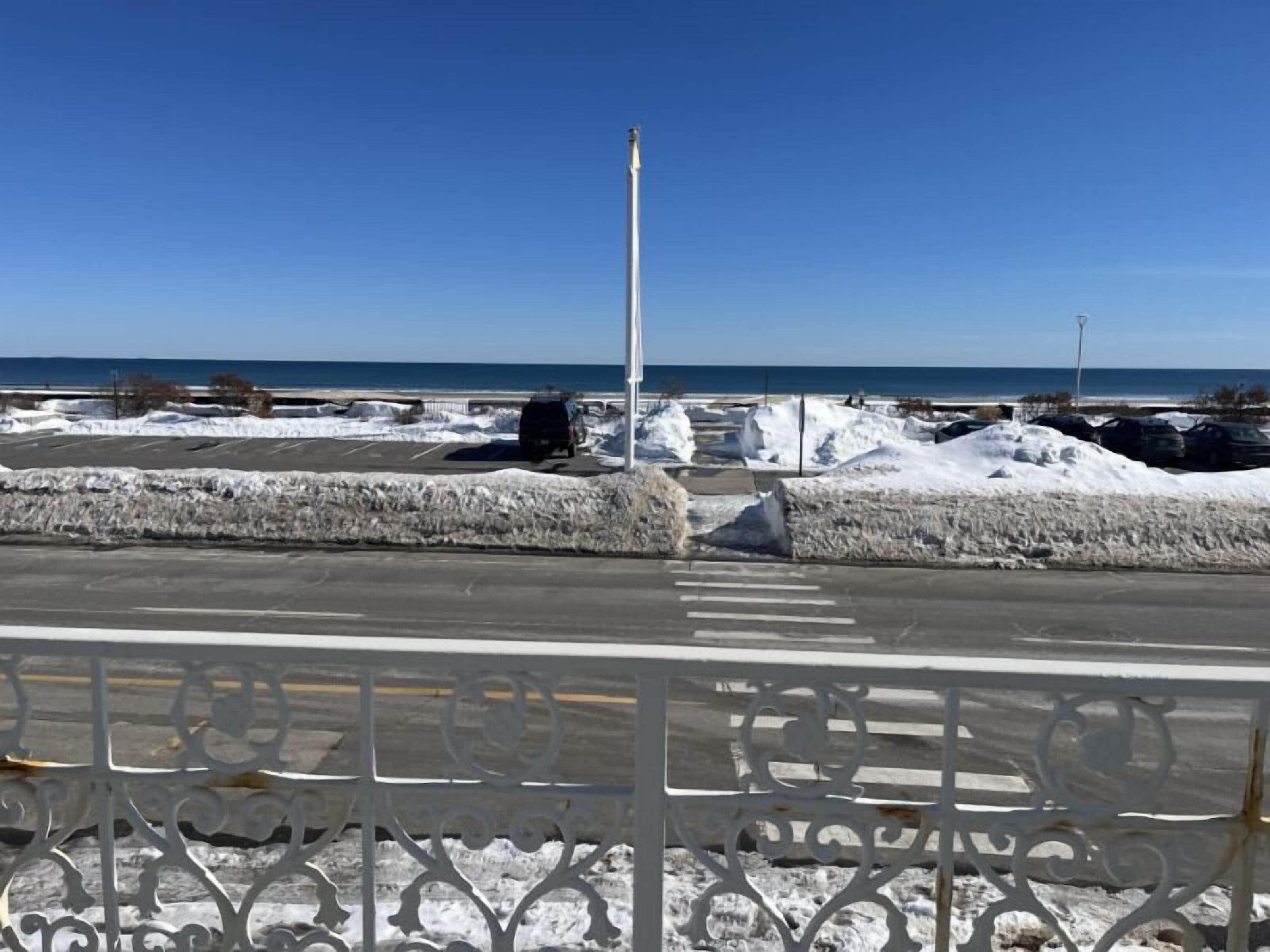 A coastal road with snow-covered barriers and a clear blue sky.