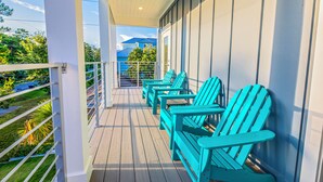 A covered balcony with wooden flooring and white railings, featuring turquoise Adirondack chairs. - Blue Horizon • Golf Cart, Pool & Sleeps 32 (Santa Rosa Beach)
