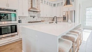 A modern kitchen with white cabinetry, stainless steel appliances, and a large island with bar stools. - Blue Horizon • Golf Cart, Pool & Sleeps 32 (Santa Rosa Beach)