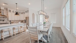 A modern kitchen with white cabinetry, a marble backsplash, and a central island. - Blue Horizon • Golf Cart, Pool & Sleeps 32 (Santa Rosa Beach)