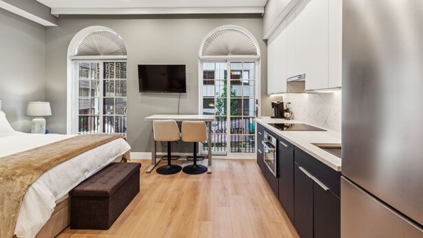 A modern hotel room with a large bed, a dining area with two chairs, a kitchen with a refrigerator, and a TV mounted on the wall. - 24 Stay Rittenhouse (Philadelphia)