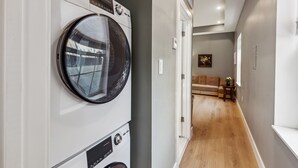 A laundry room with stacked washing machines and dryers, a wooden floor, a hallway leading to a living area with a sofa and a small table. - 24 Stay Rittenhouse (Philadelphia)