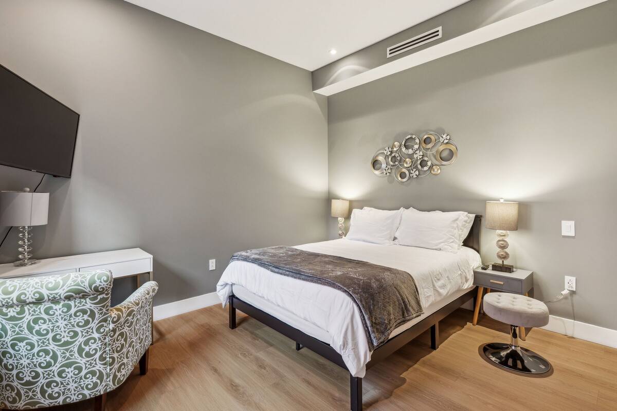 Un dormitorio con cama, lámparas de noche, una silla y un adorno en la pared.
