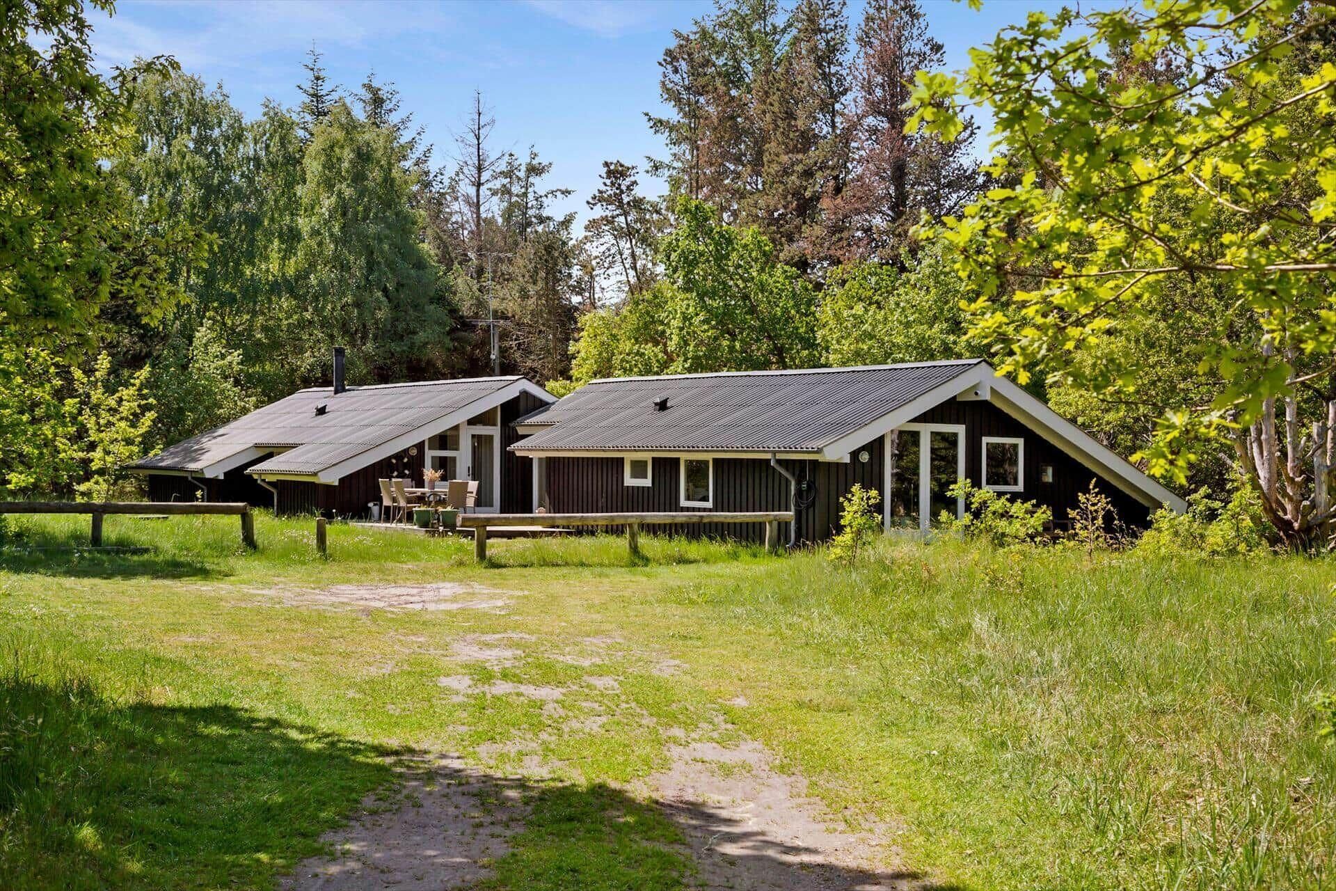 A rustic cabin with a sloped roof, surrounded by lush greenery and a clear sky.