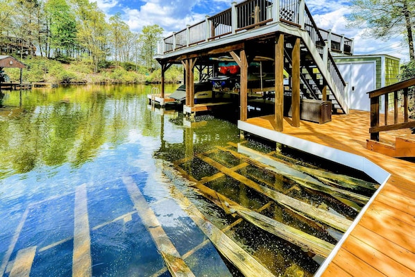 A dock extending into a calm body of water with a wooden deck and a covered area with stairs leading up to a building.