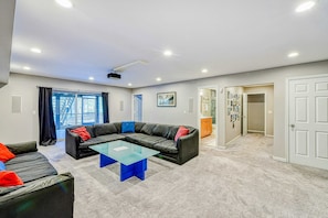 A living room with a sectional sofa, a glass coffee table, and a ceiling projector.