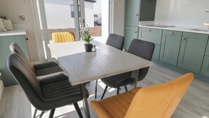 Et moderne køkken med turkise skabe, en hvid bordplade og et spiseområde med et træbord samt sorte og gule stole.