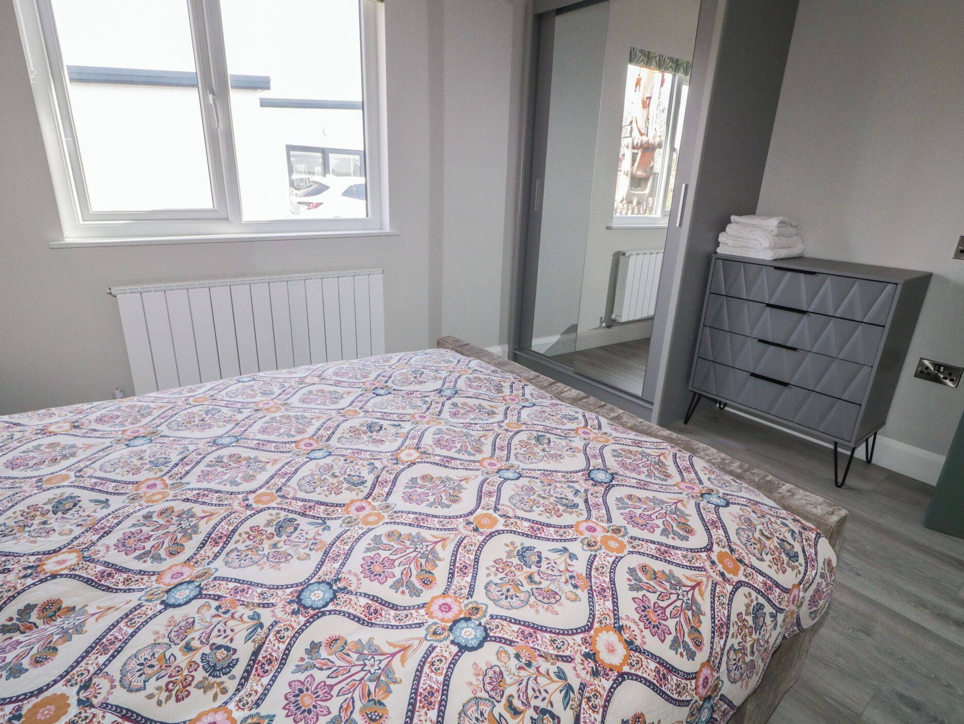 A bedroom with a bed, a dresser, a radiator, and a window.
