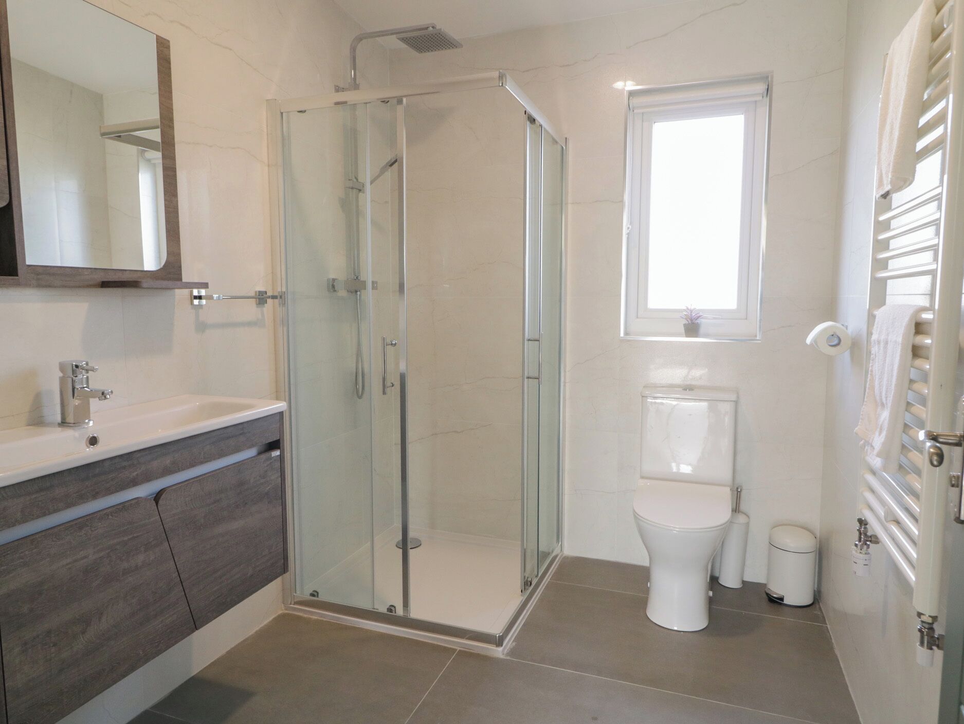 A modern bathroom with a glass-enclosed shower, a toilet, and a vanity with a mirror.
