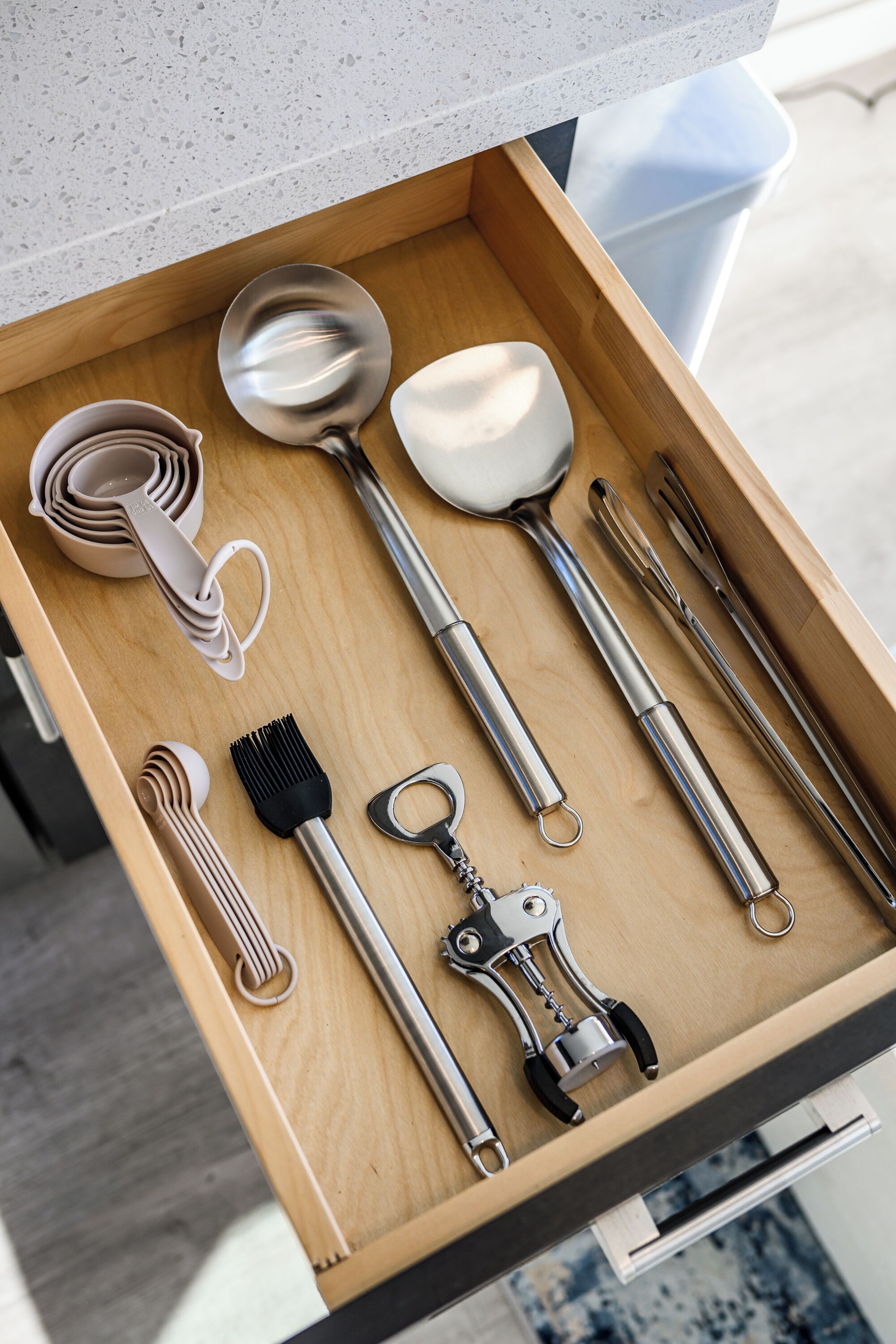 A drawer containing various kitchen utensils including a spatula, ladle, tongs, and a grater.