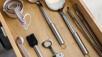 A drawer containing various kitchen utensils including a spatula, ladle, tongs, and a grater.