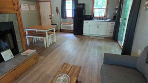 L’intérieur chaleureux d’un chalet avec un plafond en bois, une cheminée, une table à manger, un canapé et un coin cuisine équipé d’un réfrigérateur et d’un four à micro-ondes.