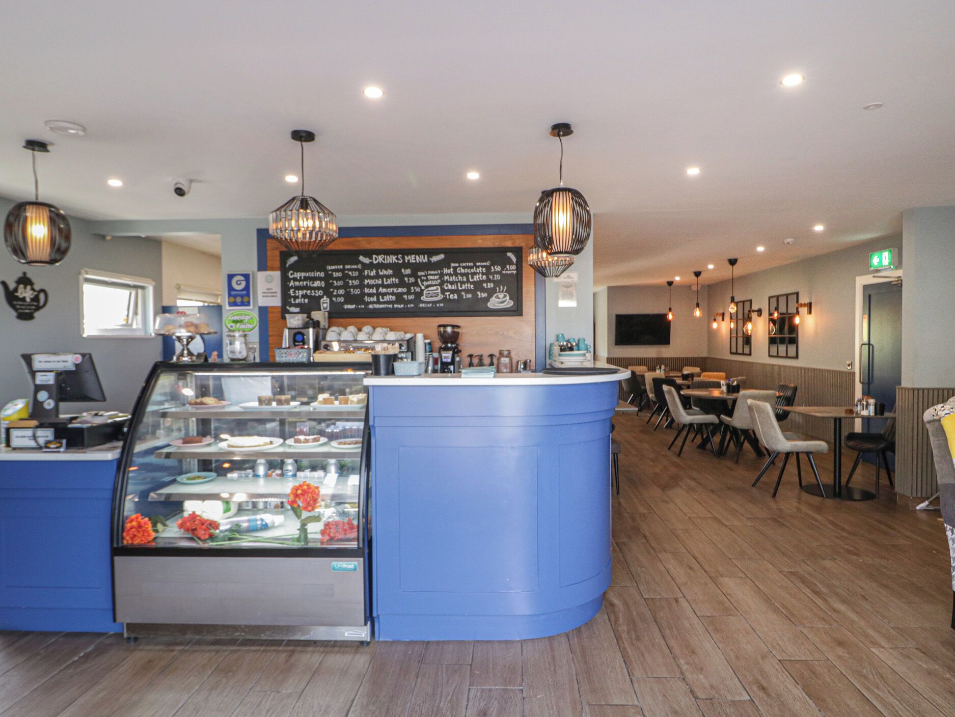 A cafe with a blue counter, a drinks menu, and a display case with pastries.