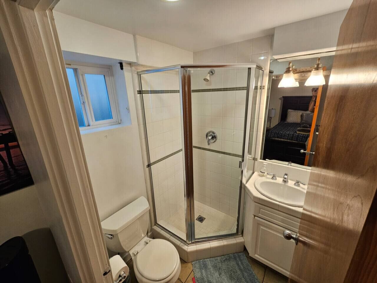 Un baño con ducha envuelta en vidrio, inodoro y lavamanos con espejo.