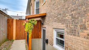 Une maison en briques avec une terrasse en bois et un pot de fleurs suspendu.