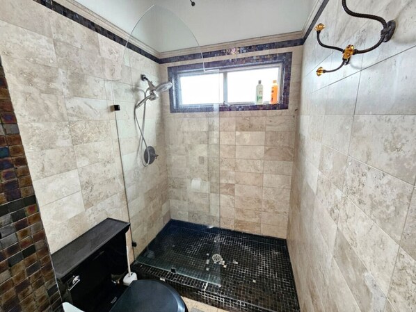A small, tiled shower room with a window, a showerhead, and a drain.