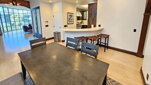 A spacious dining area with a large table and multiple chairs, a kitchen area with a bar, and a view of the outdoors through large windows.