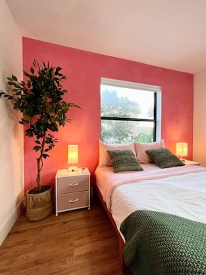 A bedroom with a bed, bedside lamps, a nightstand, a potted plant, and a window with a view.