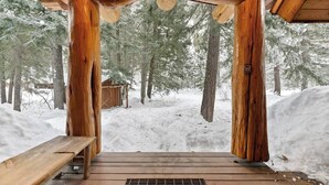 A wooden deck leading to a covered area with a view of a snowy forest. - River Front | Mountain Ski Cabin (Mazama)