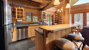 A modern kitchen with wooden cabinets, stainless steel appliances, and a bar area with stools. - River Front | Mountain Ski Cabin (Mazama)