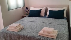 Una cama bien hecha con una colcha estampada, dos almohadas y toallas dobladas a un lado.
