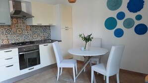 Una cocina moderna con armarios blancos, estufa a gas y salpicadero de azulejos. Hay una mesa de comedor con dos sillas blancas y un jarrón con flores.