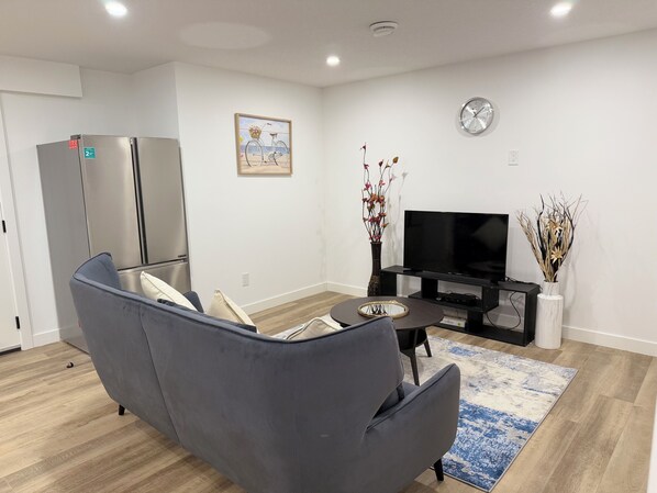 Un salon moderne avec un canapé gris, un téléviseur à écran plat, un vase décoratif et une horloge au mur.
