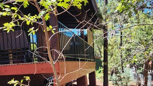 A wooden deck with a metal railing, surrounded by trees and a dirt ground. - BRAND NEW CUSTOM BUILT HOME WITH AC! FENCED FOR YOUR PUPS! (Pinetop-Lakeside)