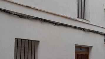 Un edificio blanco con puerta de madera marcada con el número 15, una ventana con barrotes y un pequeño balcón.
