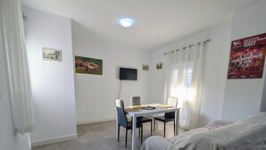 Une chambre comprenant un lit, un bureau avec une chaise, un téléviseur à écran plat et une fenêtre avec des rideaux.
