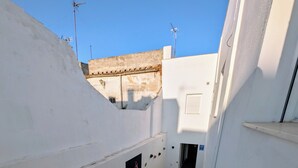Un couloir étroit au sol carrelé, aux murs blancs et sur lequel se trouve un petit tabouret en bois.