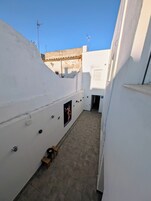 A narrow corridor with tiled flooring, white walls, and a small wooden stool.