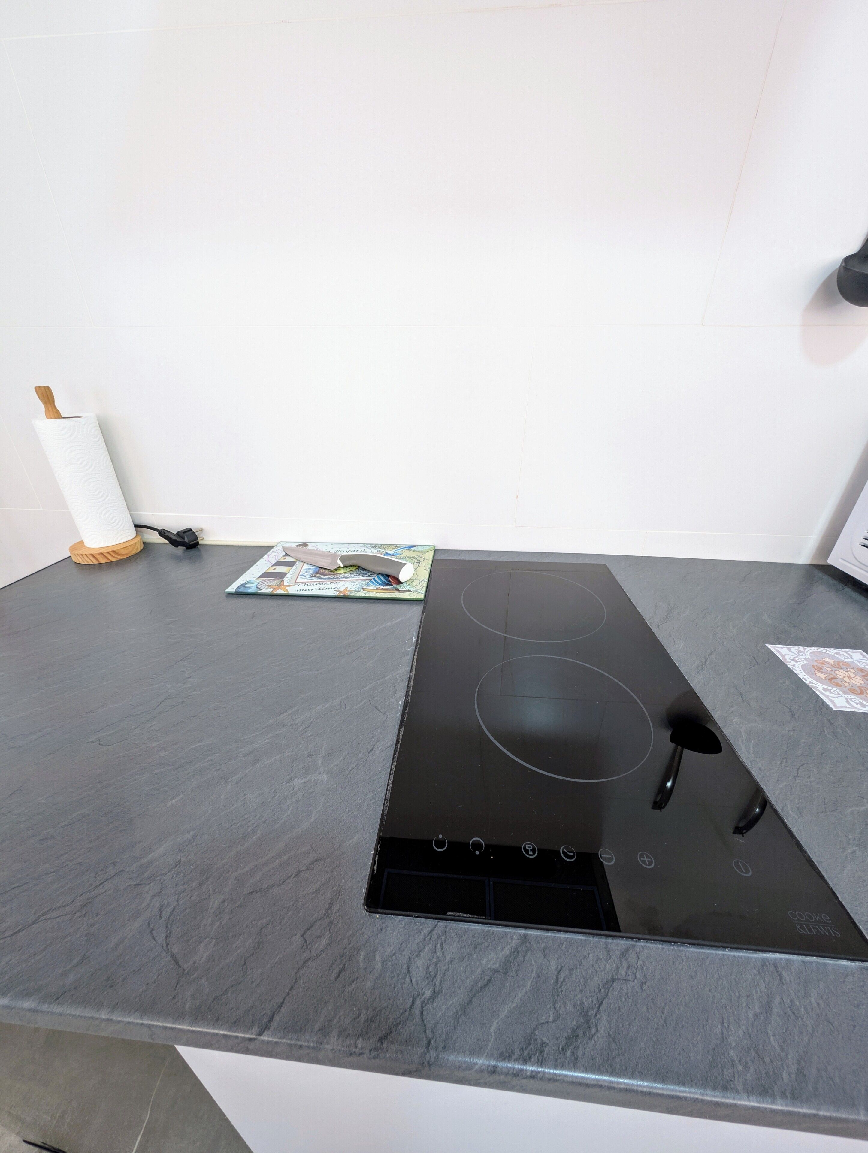 Una cocina con una placa de inducción negra, un rodillo de madera y un libro de cocina sobre la encimera.