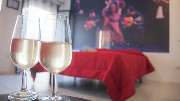 Two glasses of white wine on a table with a red tablecloth, a red sofa, and a painting of a band in the background.