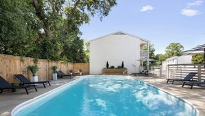 En rektangulär swimmingpool med ett trästaket och solstolar runt omkring.