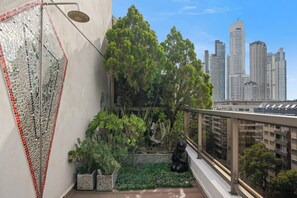 Un balcon orné d’un mur en mosaïque, agrémenté de plantes et offrant une vue sur de hauts immeubles.